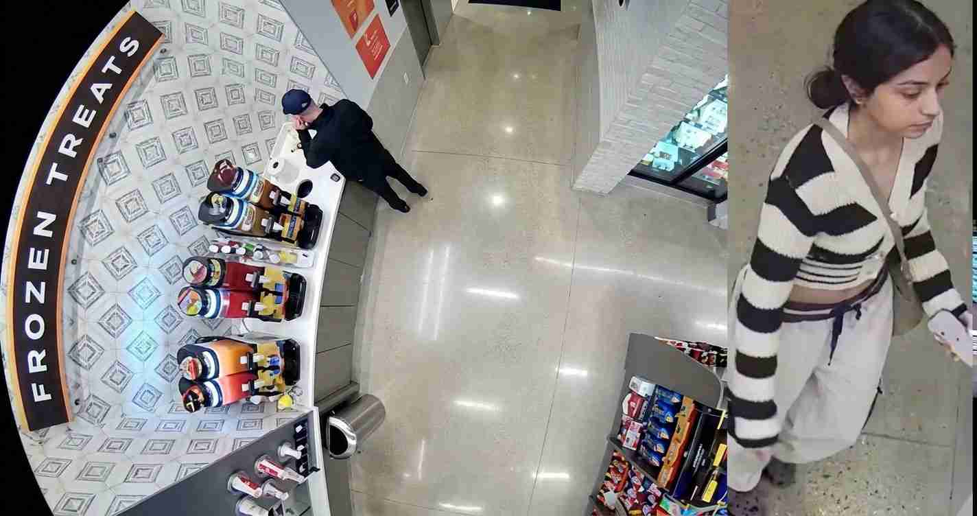 Overhead view inside a shop: a man in dark clothing at a beverage display near the counter, with shelves of drinks and a curved 'Frozen Treats' sign nearby; a woman in a striped sweater walks past with a crossbody bag.