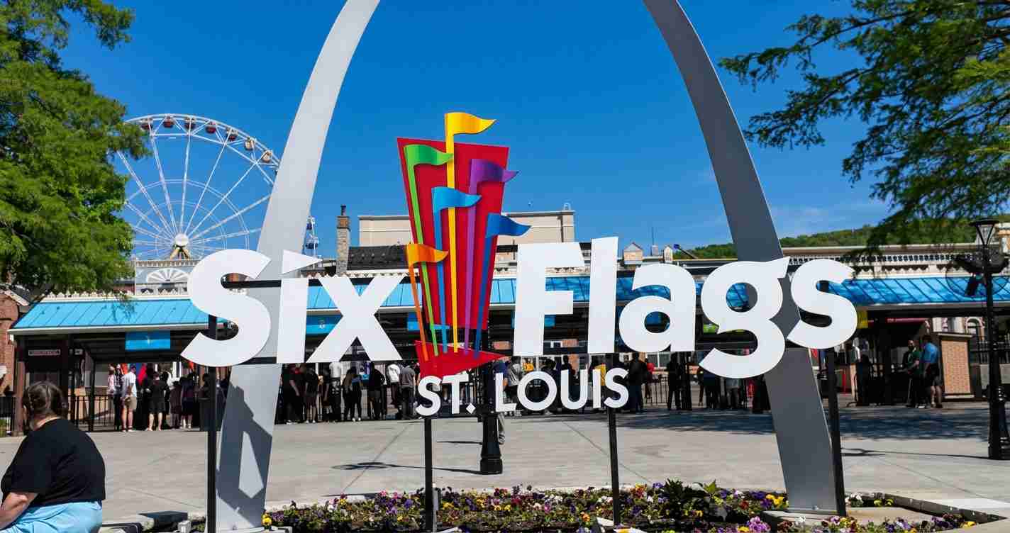 Six Flags St. Louis entrance sign with a colorful flag sculpture and a Ferris wheel in the blue sky background.
