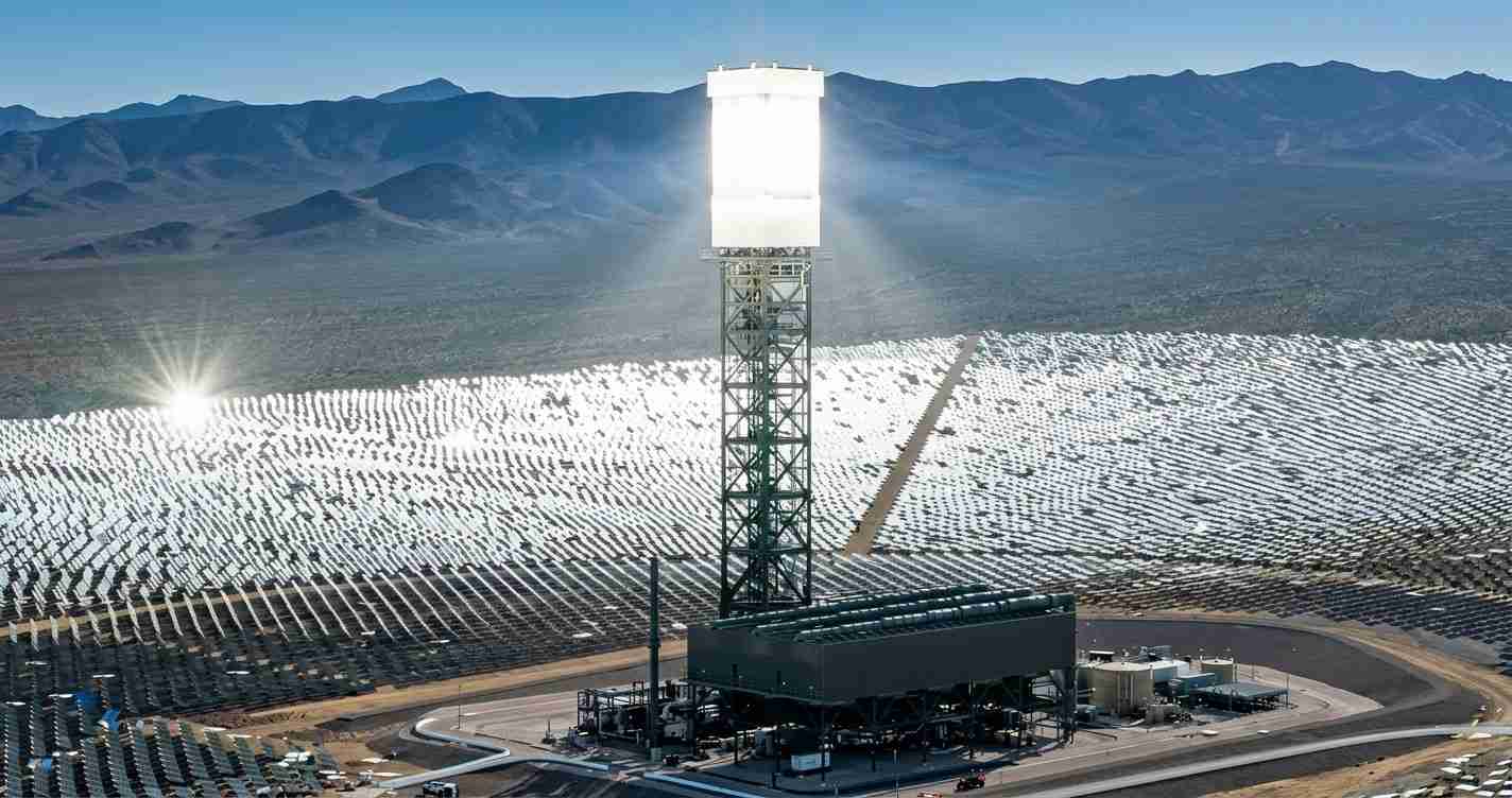 Concentrated solar power plant with a tall central receiver tower surrounded by thousands of heliostat mirrors in a desert landscape.