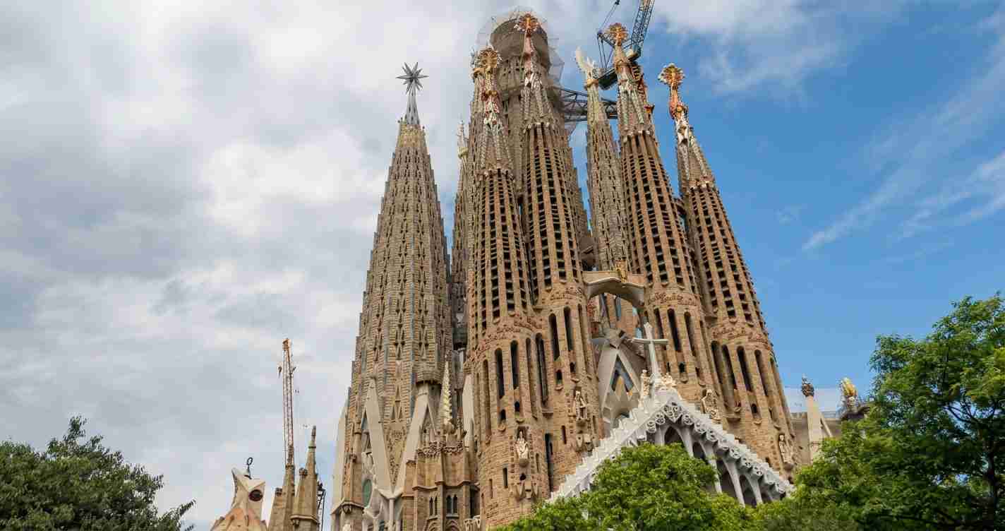Sagrada Família basilica with tall stone spires under construction, cranes visible against a blue sky.
