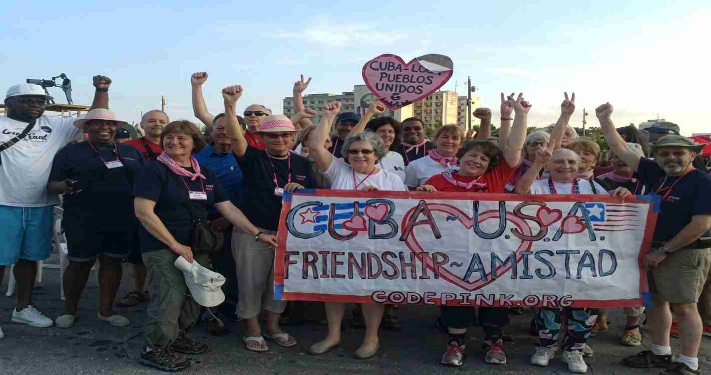 Group of diverse adults at a pro‑Cuba–USA friendship rally, holding a banner that reads 'Cuba-USA Friendship – Amistad' with hearts and flags.