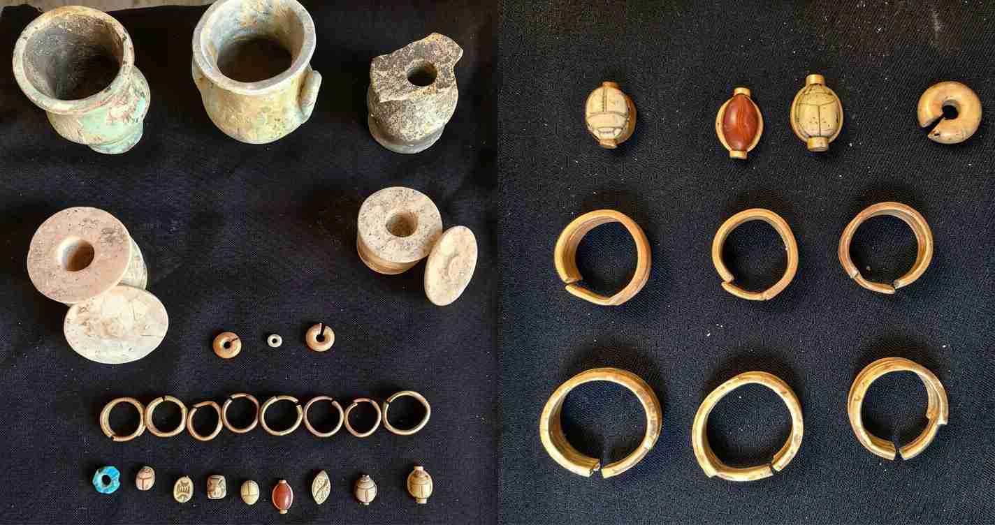 Display of ancient artifacts: clay vessels, spindle whorls, and numerous small beads laid out on black fabric.