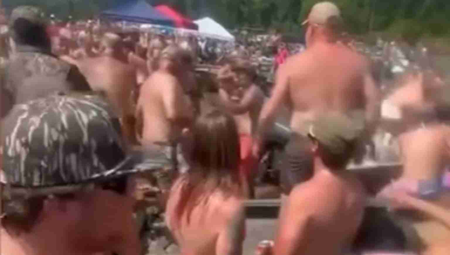 Crowded outdoor beach party with people in swimwear dancing and socializing under tents and canopies.