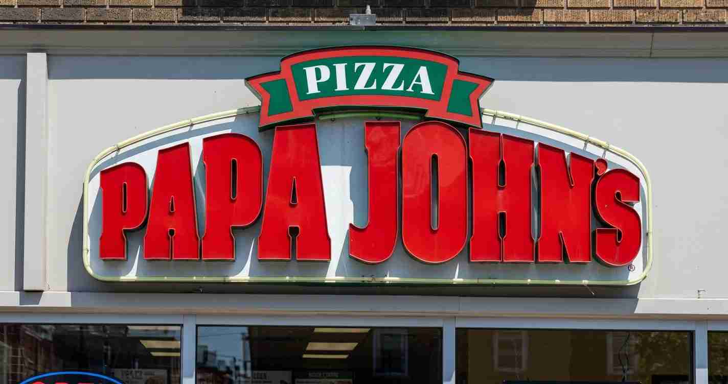 Papa John’s pizza shop storefront sign with large red letters spelling PAPA JOHNS and a green PIZZA banner above.