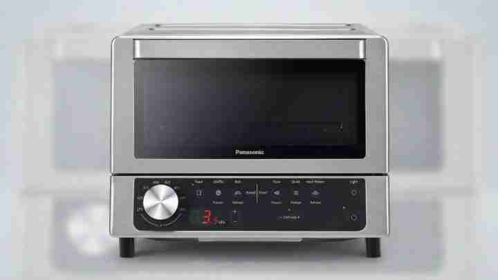 Stainless steel Panasonic toaster oven with a large black glass door on top and a control panel beneath, on a counter.