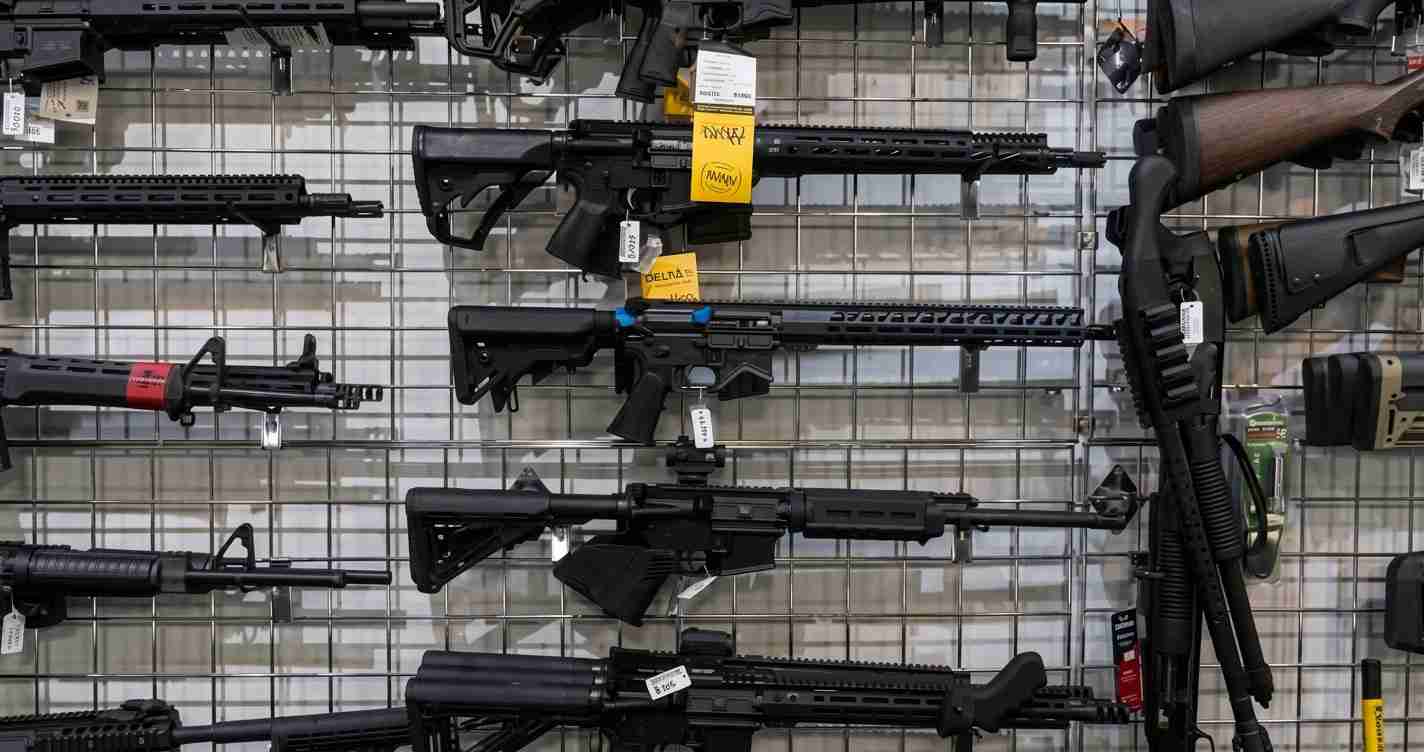 Rack of modern rifles on a metal grid wall in a gun shop, with price tags on each firearm.