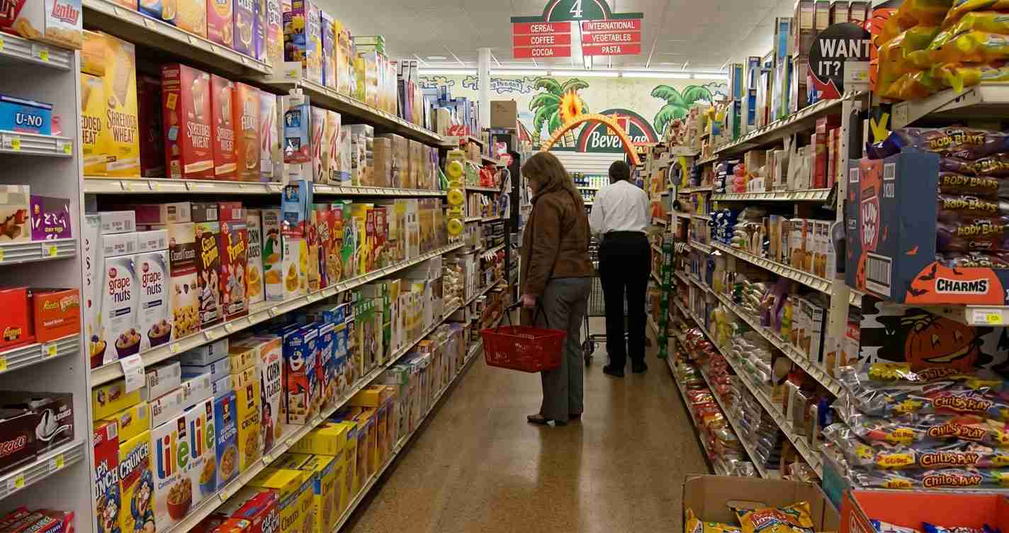 Shoppers browse cereal boxes in a supermarket aisle; a woman with a red basket stands in the center.