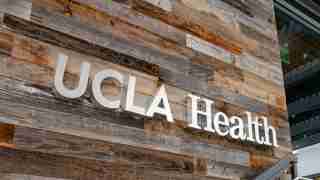 UCLA Health sign mounted on a rustic wood-paneled exterior wall outside a building.