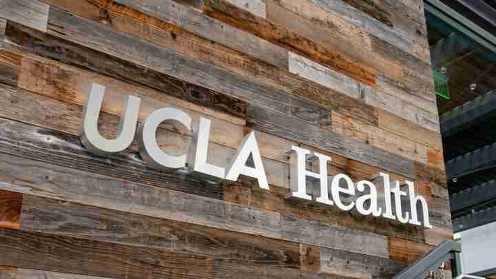 UCLA Health sign mounted on a rustic wood-paneled exterior wall outside a building.